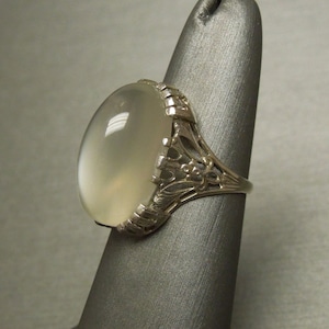 May include: A silver ring with an oval-shaped moonstone set in a filigree design.