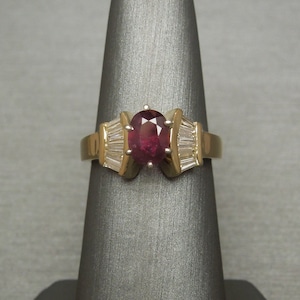 May include: A gold ring with a large oval ruby gemstone surrounded by smaller baguette-cut diamonds.