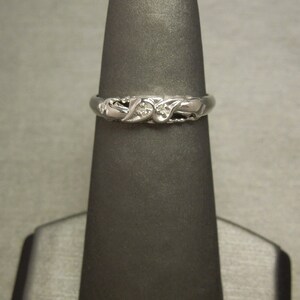 May include: A silver ring with a delicate design featuring two small diamonds. The ring is on a black ring display stand.