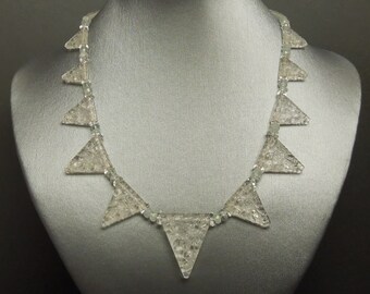 May include: A necklace made of clear glass triangle beads with a textured surface. The necklace is displayed on a gray mannequin bust.