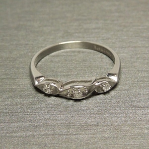 May include: A silver band ring with a delicate design featuring three small diamonds set in the band.