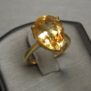 May include: A gold ring featuring a pear-shaped topaz gemstone. The gemstone is a pale yellow colour.