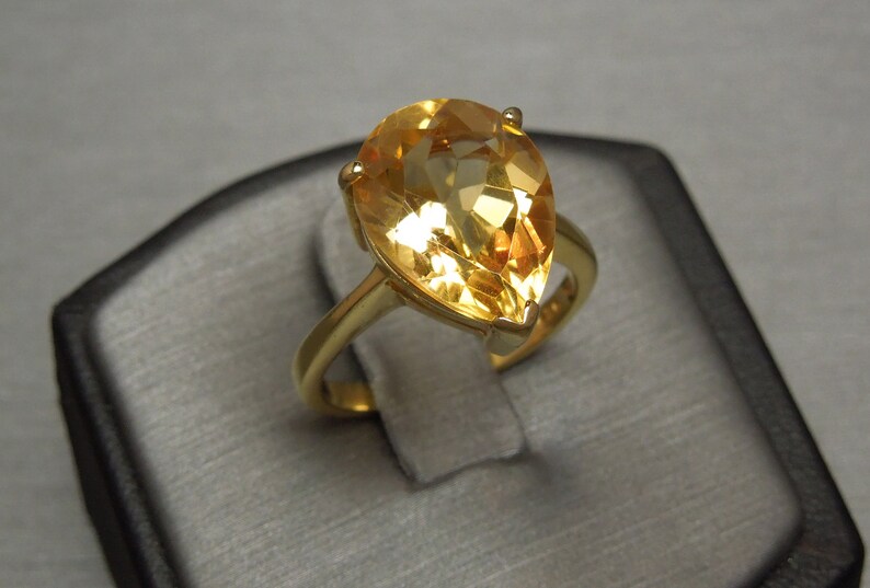 May include: A gold ring featuring a pear-shaped topaz gemstone. The gemstone is a pale yellow colour.