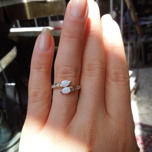 K&ouml;nnte beinhalten: Ein goldener Ring mit zwei wei&szlig;en Opal-Steinen, die in Tropfenform gefasst sind. Der Ring ist mit kleinen Diamanten auf der Ringschiene besetzt.