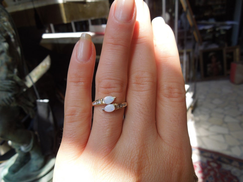 K&ouml;nnte beinhalten: Ein goldener Ring mit zwei wei&szlig;en Opal-Steinen, die in Tropfenform gefasst sind. Der Ring ist mit kleinen Diamanten auf der Ringschiene besetzt.
