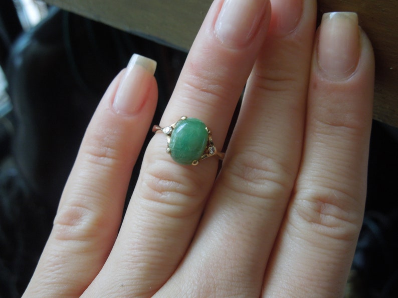 K&ouml;nnte beinhalten: Ein goldener Ring mit einem gr&uuml;nen ovalen Edelstein und kleinen klaren Edelsteinen auf der Ringschiene.