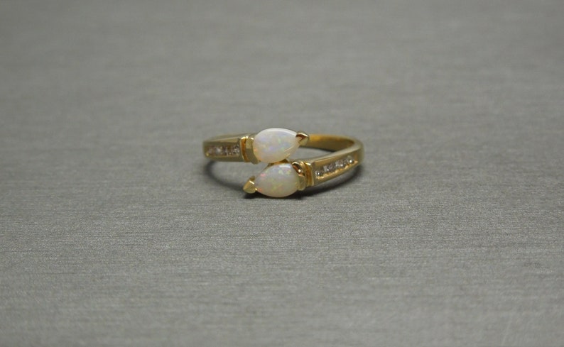K&ouml;nnte beinhalten: Ein goldener Ring mit zwei birnenf&ouml;rmigen Opalen und einer Reihe kleiner Diamanten.