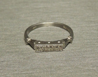 May include: A silver ring with a row of five small diamonds set in a rectangular shape.
