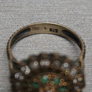 Pu&ograve; includere: Un anello d'argento con una montatura di pietre verdi e bianche. L'interno della fascia &egrave; timbrato con il numero "925".