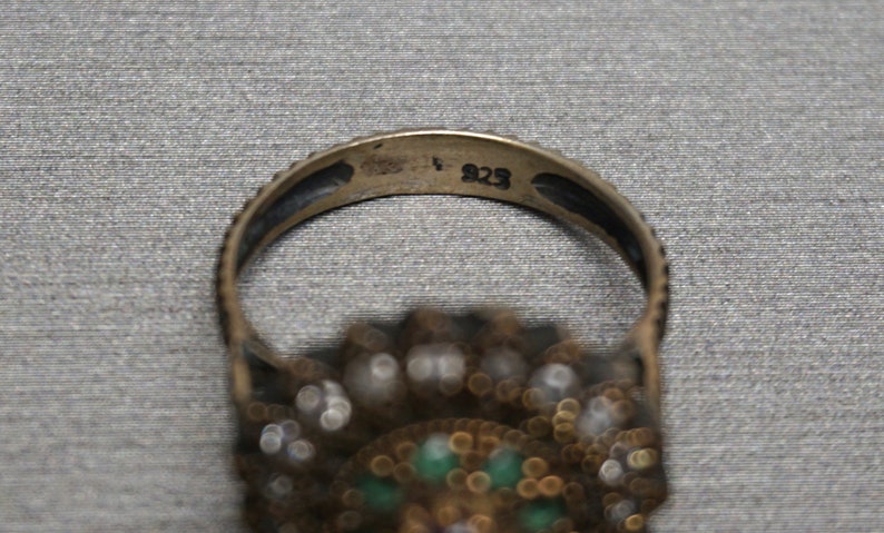 Pu&ograve; includere: Un anello d'argento con una montatura di pietre verdi e bianche. L'interno della fascia &egrave; timbrato con il numero "925".