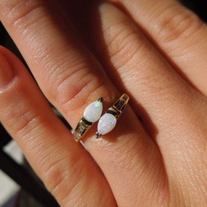 K&ouml;nnte beinhalten: Ein goldener Ring mit zwei birnenf&ouml;rmigen wei&szlig;en Opalen und kleinen klaren Steinen, die in die Band gefasst sind.