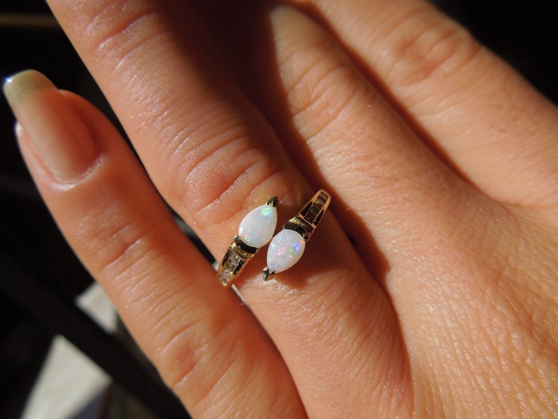 K&ouml;nnte beinhalten: Ein goldener Ring mit zwei birnenf&ouml;rmigen wei&szlig;en Opalen und kleinen klaren Steinen, die in die Band gefasst sind.