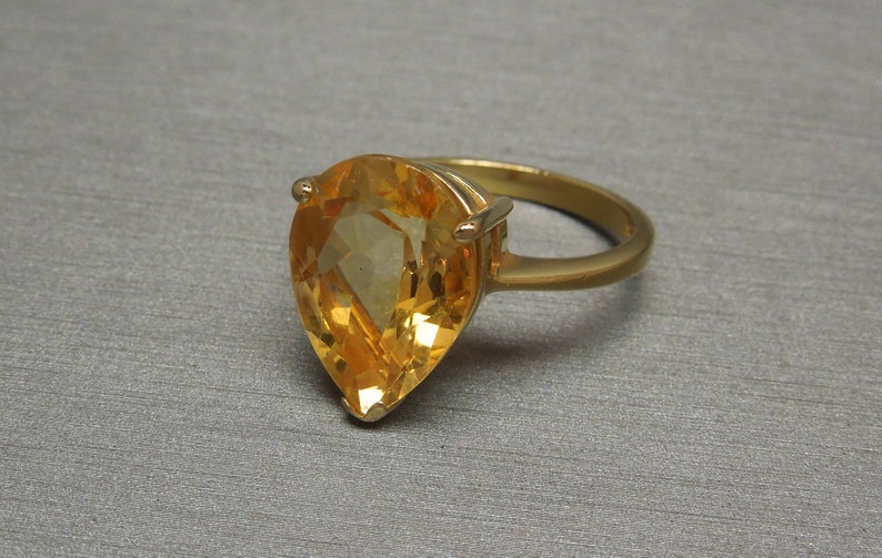 May include: A gold ring featuring a large pear-shaped topaz gemstone. The gemstone is a light orange colour and has a faceted cut.