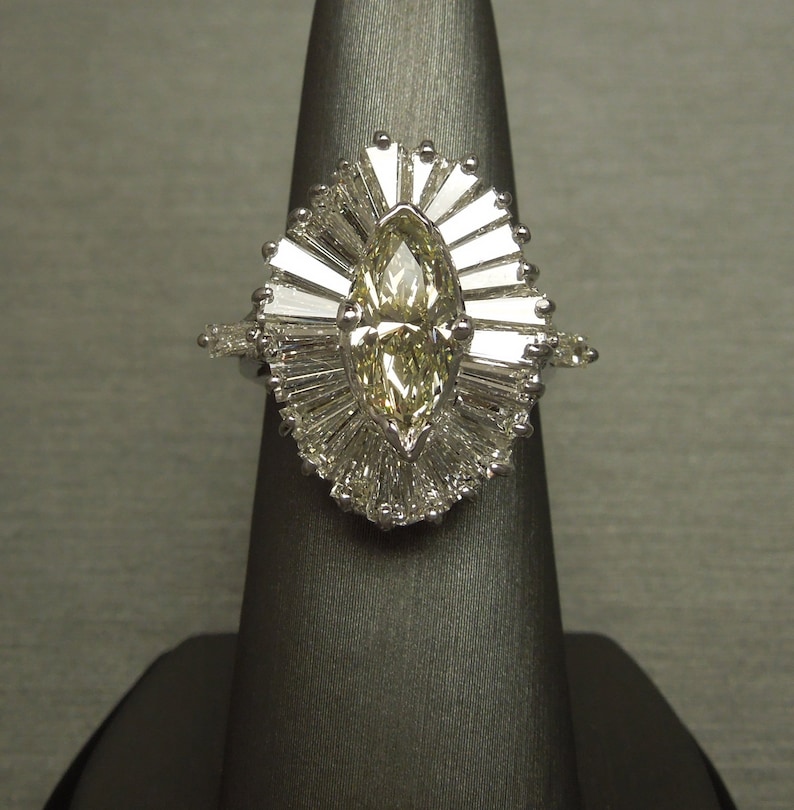 Op de afbeelding: Een ring van witgoud met een marquise geslepen diamant en een halo van baguette diamanten.