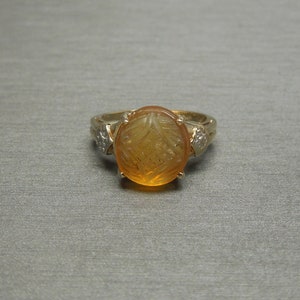 May include: A gold ring with a carved amber stone and two small diamonds on the band.