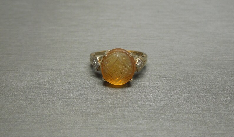 May include: A gold ring with a carved amber stone and two small diamonds on the band.