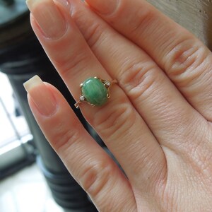 K&ouml;nnte beinhalten: Ein goldener Ring mit einem gr&uuml;nen ovalen Edelstein und zwei kleinen Diamanten auf der Ringschiene.