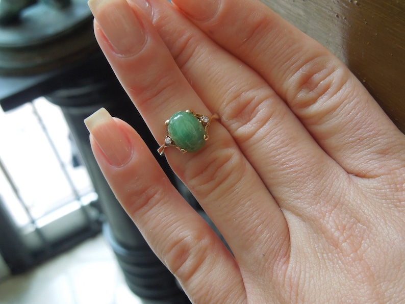 K&ouml;nnte beinhalten: Ein goldener Ring mit einem gr&uuml;nen ovalen Edelstein und zwei kleinen Diamanten auf der Ringschiene.