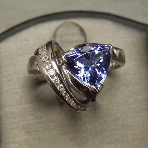 May include: A silver ring with a large, triangular, blue gemstone surrounded by smaller, white gemstones.