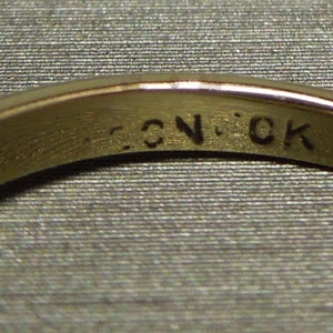 May include: Close-up of the inside of a gold ring with the inscription "C.N.CK" engraved on the band.