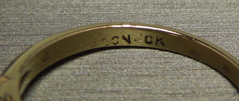 May include: Close-up of the inside of a gold ring with the inscription "C.N.CK" engraved on the band.