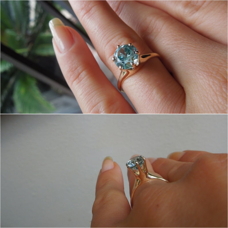 May include: A gold ring with a large, round, light blue gemstone set in a prong setting.