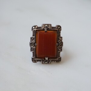 May include: A silver ring with a rectangular orange stone set in a geometric frame.