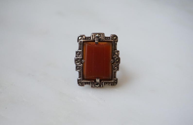 May include: A silver ring with a rectangular orange stone set in a geometric frame.