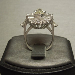 Op de afbeelding: Een zilveren ring met een grote, ovale, gele edelsteen omringd door kleinere, baguettevormige diamanten.