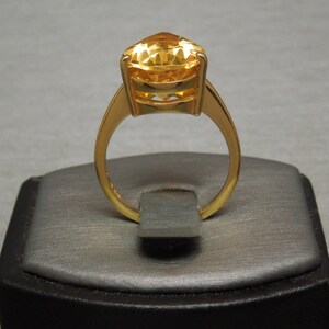 May include: A gold ring featuring a large, faceted, yellow gemstone set in a gold band.