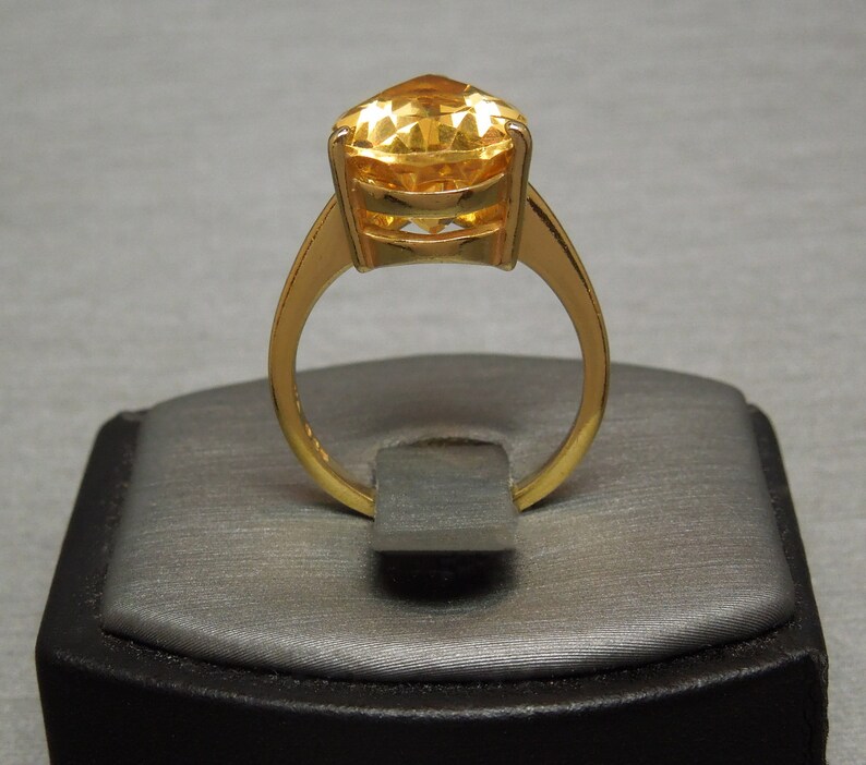May include: A gold ring featuring a large, faceted, yellow gemstone set in a gold band.