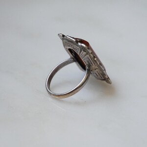 May include: A silver ring with a geometric design and a brown stone in the center.