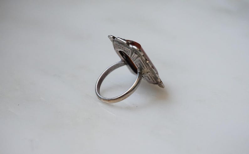 May include: A silver ring with a geometric design and a brown stone in the center.