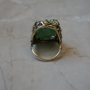 May include: A green jade ring with a detailed gold setting. The ring is set with a carved jade stone and has a delicate floral design.