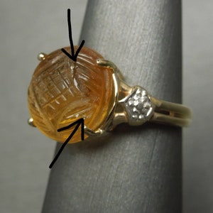 May include: A gold ring with a carved amber stone and a small diamond accent. The stone has a geometric pattern carved into it.