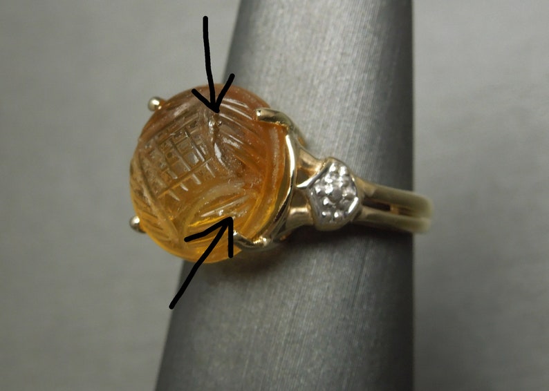 May include: A gold ring with a carved amber stone and a small diamond accent. The stone has a geometric pattern carved into it.