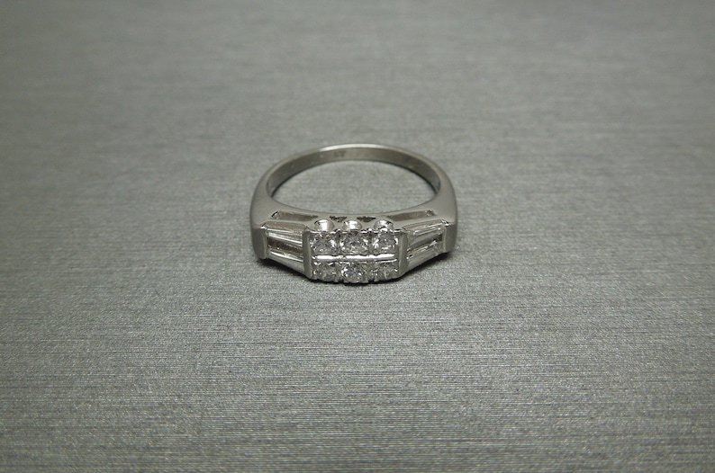 May include: A silver ring featuring a row of small diamonds set in a channel setting. The ring has a simple, elegant design.