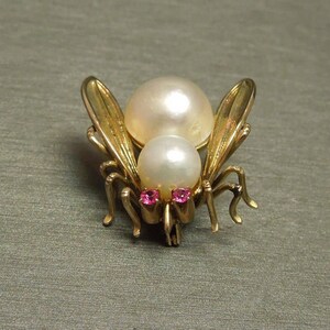 May include: A gold tone brooch featuring a stylized insect with two pearl-like accents and two pink rhinestones for eyes.