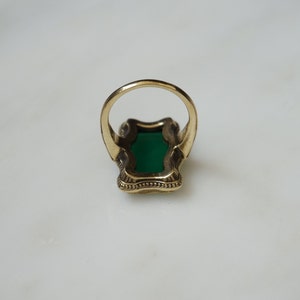 May include: A gold ring with a large green stone set in a decorative, ornate setting.