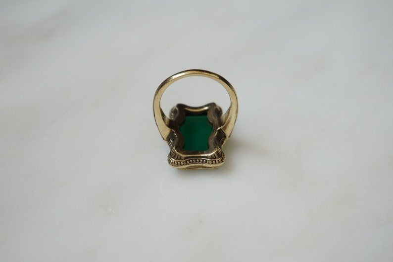May include: A gold ring with a large green stone set in a decorative, ornate setting.