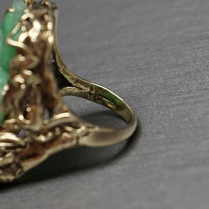 May include: A gold ring with a green jade stone set in a floral design.