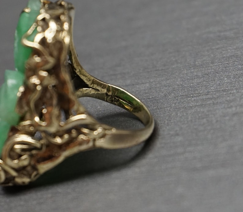 May include: A gold ring with a green jade stone set in a floral design.