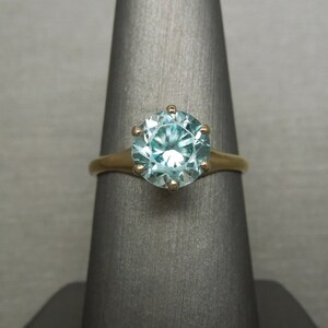 May include: A gold ring with a large, round, light blue gemstone set in a six-prong setting.