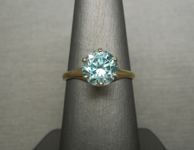 May include: A gold ring with a large, round, light blue gemstone set in a six-prong setting.