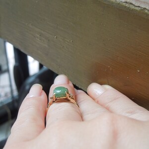 K&ouml;nnte beinhalten: Ein goldener Ring mit einem gr&uuml;nen Edelstein und zwei kleineren Diamanten auf der Ringschiene.
