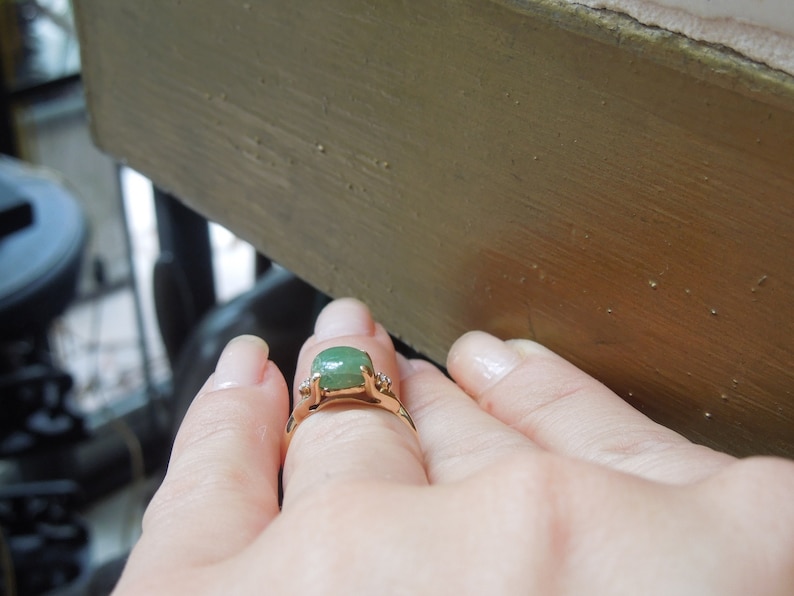 K&ouml;nnte beinhalten: Ein goldener Ring mit einem gr&uuml;nen Edelstein und zwei kleineren Diamanten auf der Ringschiene.
