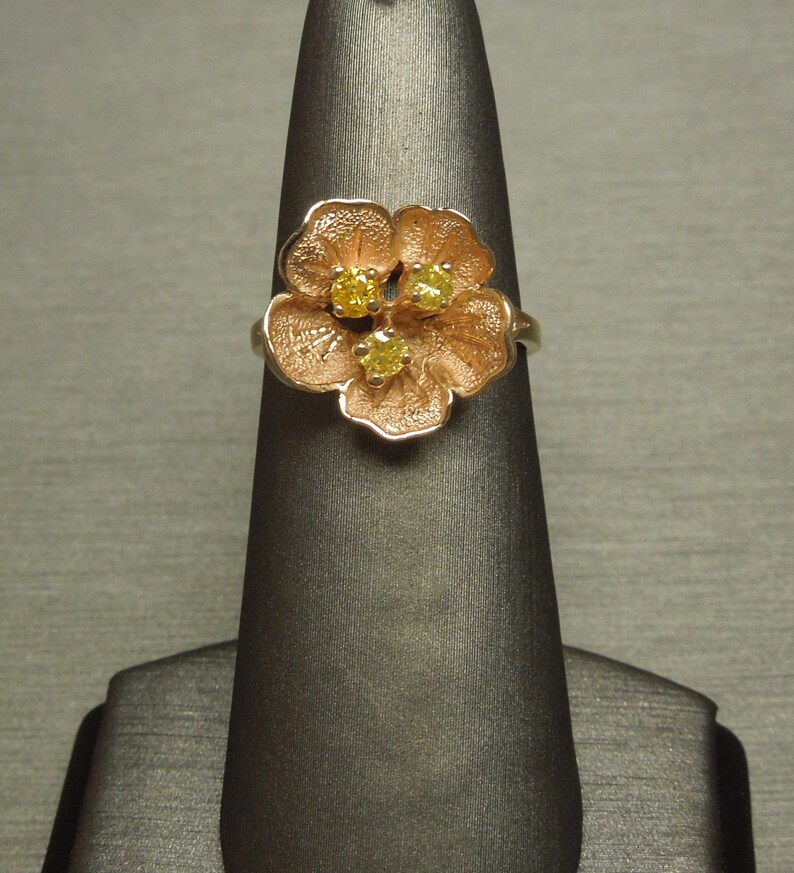 May include: A gold ring with a flower design featuring three yellow gemstones.