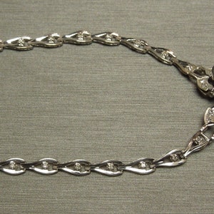 K&ouml;nnte beinhalten: Eine silberne Halskette mit einem gro&szlig;en, rechteckigen, hellblauen Edelsteinanh&auml;nger. Der Anh&auml;nger ist von kleineren Diamanten umgeben. Die Kette hat ein filigranes Design mit kleinen, tropfenf&ouml;rmigen Gliedern, jeweils mit einem kleinen Diamanten.