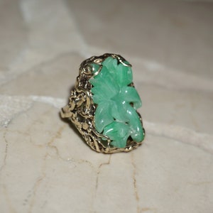May include: A green jade ring with a carved flower design set in a gold filigree setting.