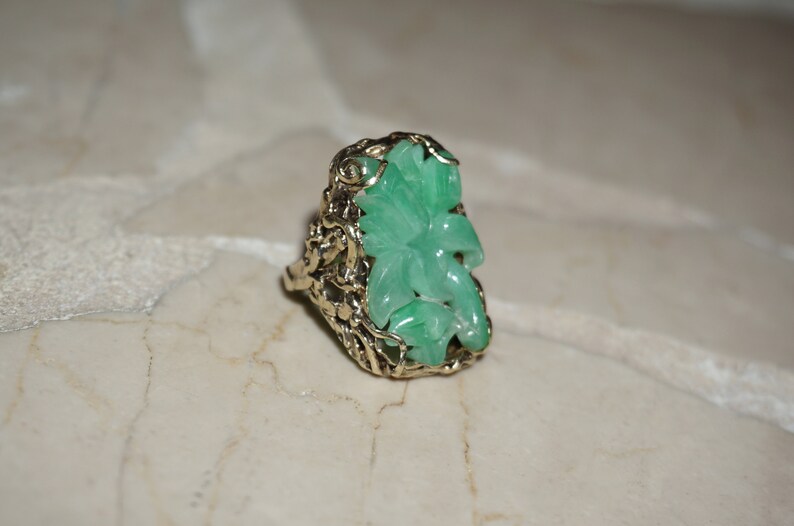 May include: A green jade ring with a carved flower design set in a gold filigree setting.